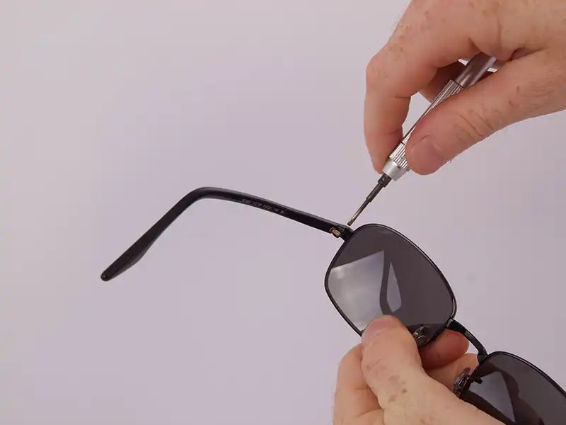Hands tighten a screw on black sunglasses with a small screwdriver