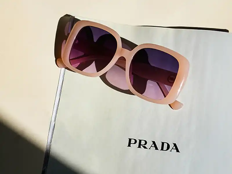 Pink oversized Prada sunglasses with purple lenses resting on a Prada-branded magazine page