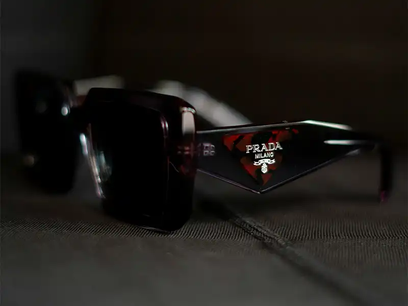 Close-up of a Prada Milano logo on the arm of dark sunglasses, emphasizing branding details used to authenticate real Prada sunglasses