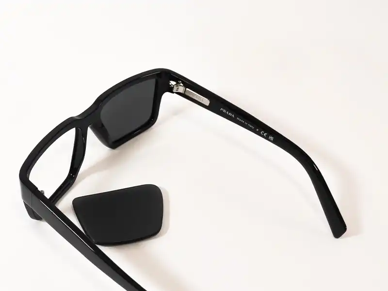 Disassembled Prada sunglasses showing a removed Prada lens and inner arm details, highlighting authenticity markings and easy lens replacement