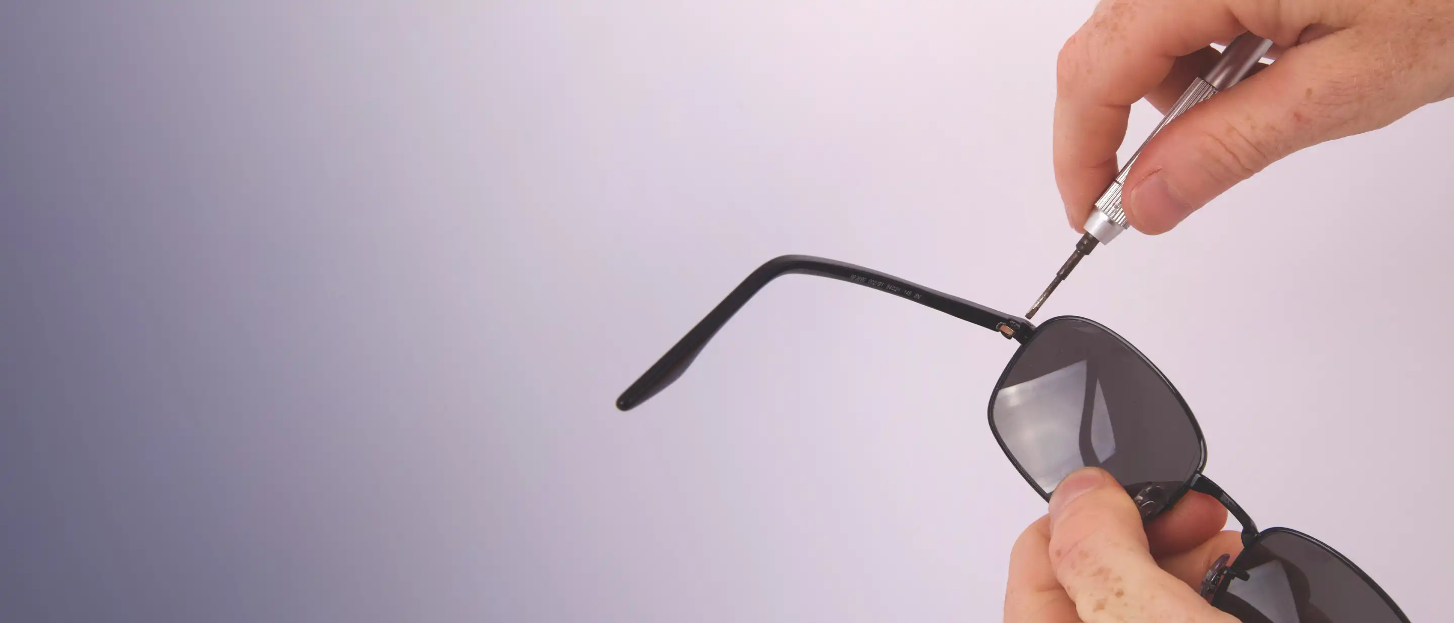 Hand die eine Sonnenbrille hält und eine andere Hand die einen Schraubendreher benutzt Hand die eine Sonnenbrille hält und eine andere Hand die einen Schraubendreher benutzt