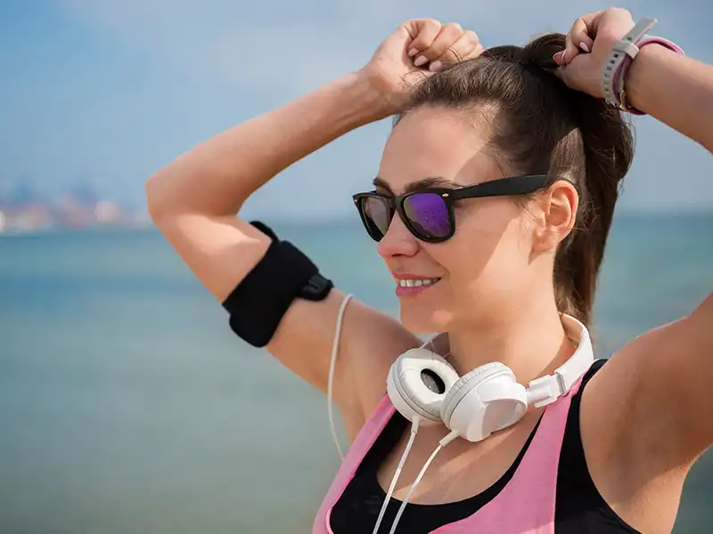 Frau im sportlichen Outfit mit schwarzer Sonnenbrille mit verspiegelten Gläsern am Strand.