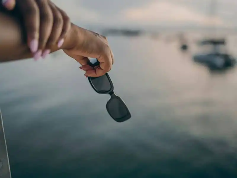 Hände halten eine schwimmende schwarze Sonnenbrille über offenem Wasser