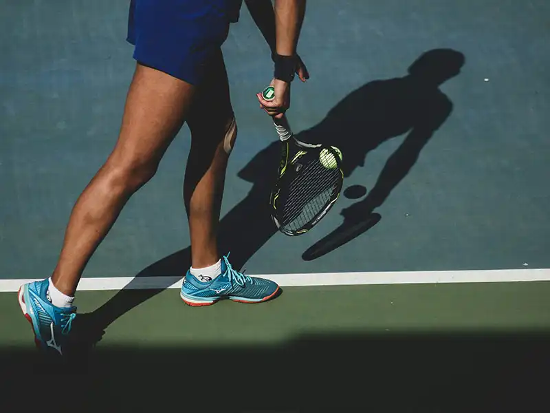 Nahaufnahme von Tennisball und Schläger auf dem Platz, die Schatten und visuellen Kontrast zeigt