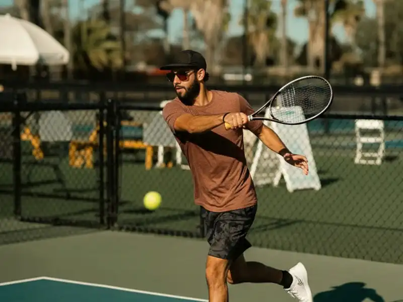 Tennisspieler schlägt eine Vorhand auf einem Hartplatz und verfolgt den Ball bei hellem Licht.
