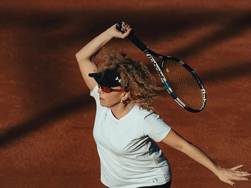 Tennisspieler trägt Sonnenbrille auf einem Sandplatz bei warmen Lichtverhältnissen