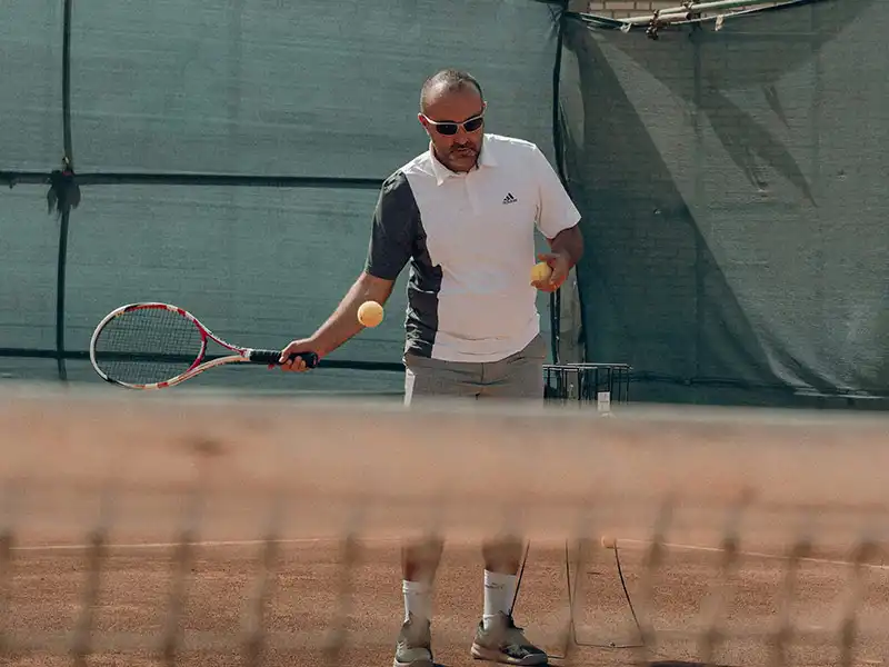 Tennisspieler trägt Sonnenbrille und bereitet sich auf den Schlag vor.