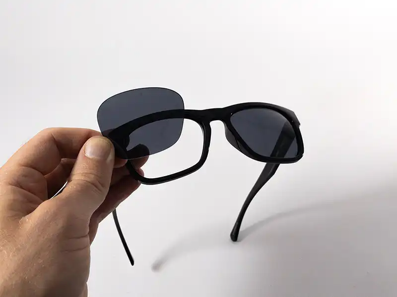 Person hält und setzt Ersatzgläser in schwarze Vollrahmen-Sonnenbrille ein