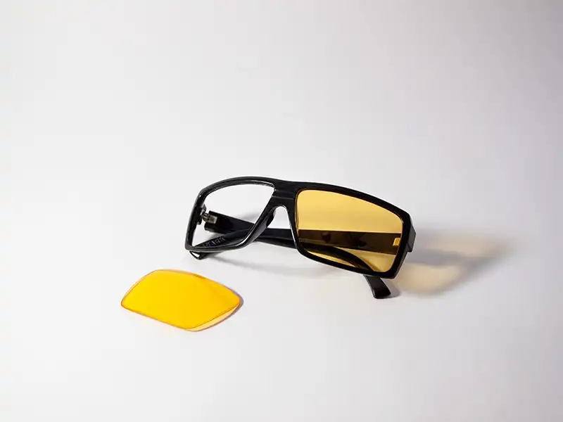 Schwarze Sonnenbrille mit austauschbaren gelben Gläsern, die den Austausch der Gläser als intelligentes und nachhaltiges Style-Upgrade hervorheben.