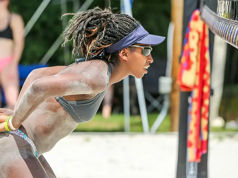 Jugadora de voleibol de playa usando gafas deportivas oscuras y visera, concentrada durante un partido.