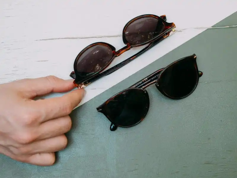 Una mano sostiene dos pares de gafas de sol carey sobre una superficie verde y blanca.