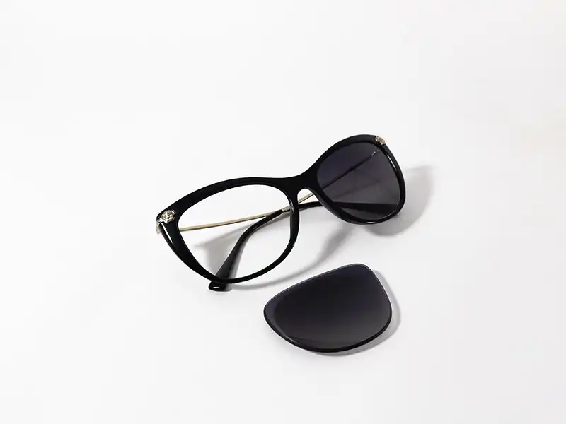 Gafas de sol negras de estilo ojo de gato, con una lente oscura removida, sobre un fondo blanco.