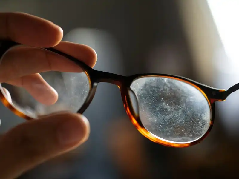 Une main tient des lunettes écaille avec des verres tachés