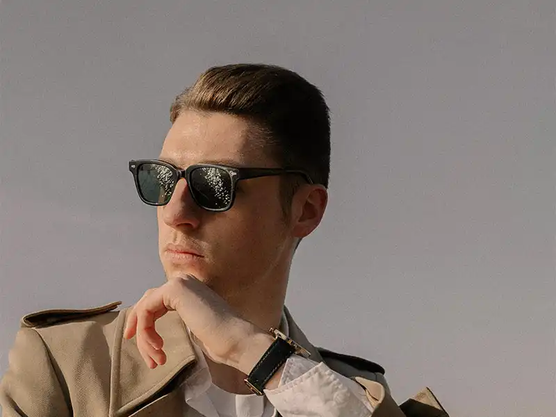 Homme portant des lunettes rectangulaires noires avec une monture en acétate épaisse, reflétant la lumière, représentant un style intemporel classique Homme portant des lunettes rectangulaires noires avec une monture en acétate épaisse, reflétant la lumière, représentant un style intemporel classique