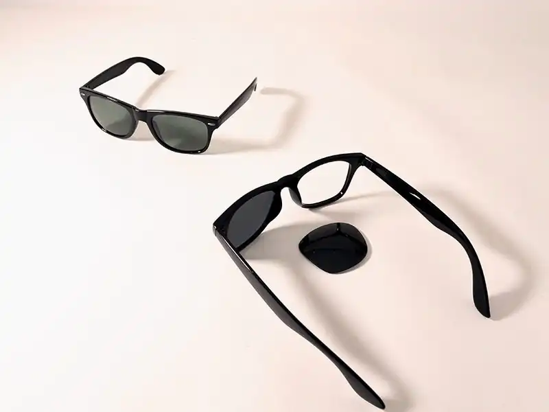 Deux lunettes Wayfarer noires classiques sur fond clair, avec un verre retiré pour illustrer le remplacement des verres Deux lunettes Wayfarer noires classiques sur fond clair, avec un verre retiré pour illustrer le remplacement des verres
