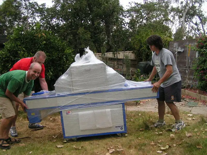 Craig and his neighbours carrying a small lens cutter machine in Craig’s backyard.