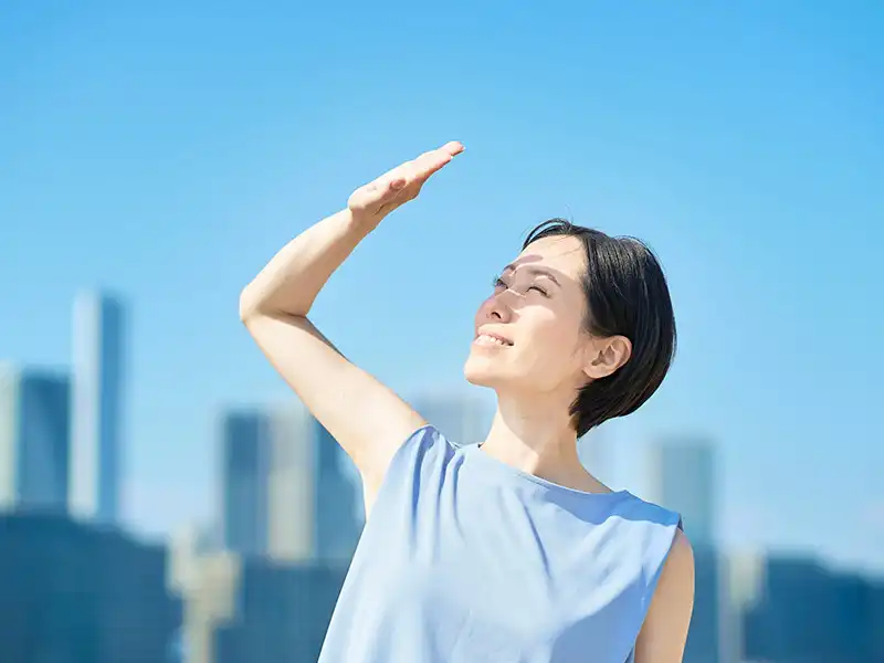 Une femme plissant les yeux sous un soleil éclatant, illustrant la nécessité de lunettes de soleil photophobes pour gérer l'éblouissement et la sensibilité des yeux.