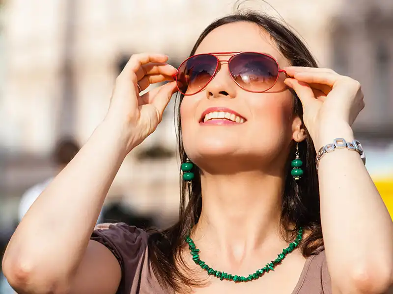 Une femme portant joyeusement de grandes lunettes de soleil aviateur, montrant comment les lunettes de soleil adaptées aux yeux sensibles offrent confort et soulagement en plein soleil.
