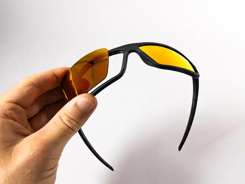 Une main remplace la lentille d'une paire de lunettes de soleil enveloppantes, montrant comment mettre à niveau les montures avec de nouvelles lentilles personnalisées pour la sensibilité à la lumière.
