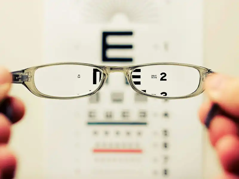Eyeglasses held up, focusing letters on an eye chart during an annual eye exam.