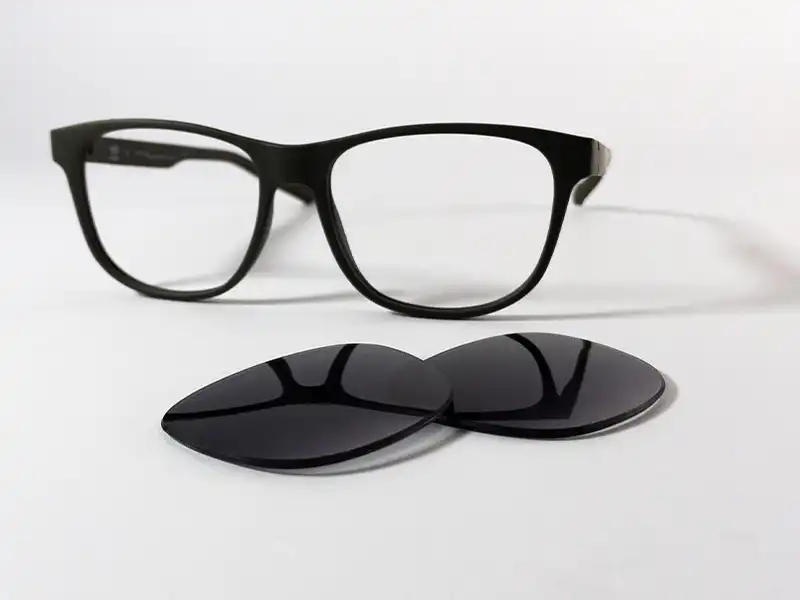 Black sunglasses frame with replacement lenses placed in front, showing a lens replacement setup