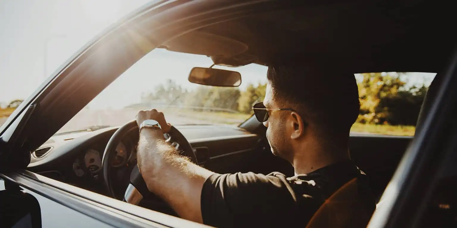 A man driving a car in the sun wearing metal framed aviator style sunglasses