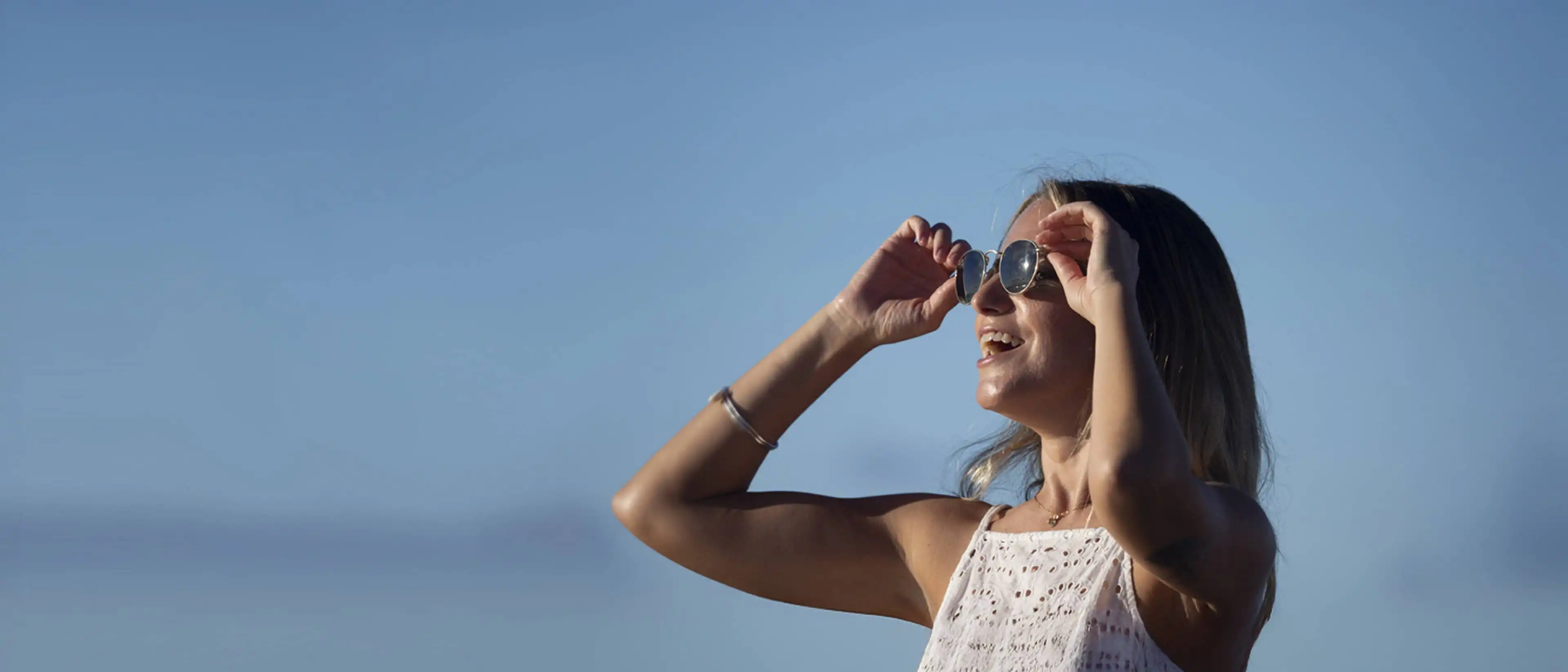 A woman looking into the distance putting on her sunglasses with new frames